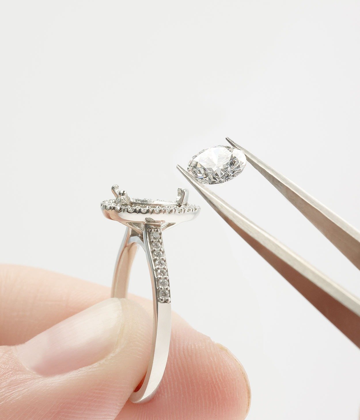 A goldsmith holding up a single round brilliant cut diamond against a mount.