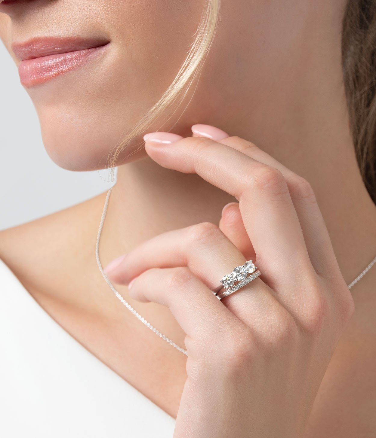 A lady wearing a platinum three stone diamond engagement ring and diamond wedding band