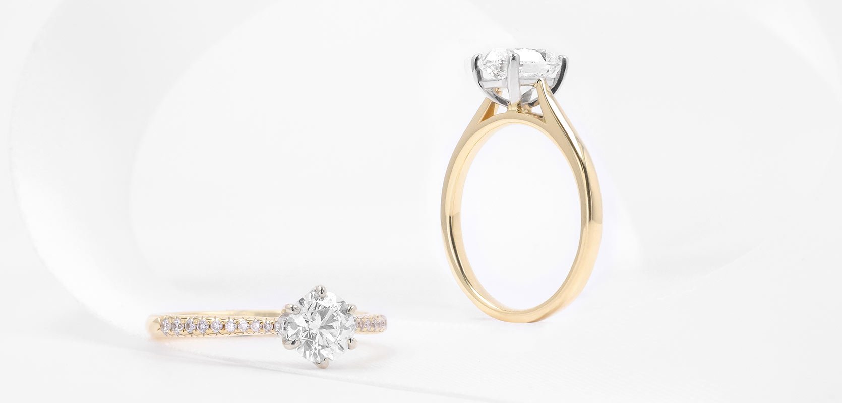 Two diamond engagement rings, with a round brilliant cut centre diamond and diamonds set along the shoulders of the 18ct yellow gold band. 