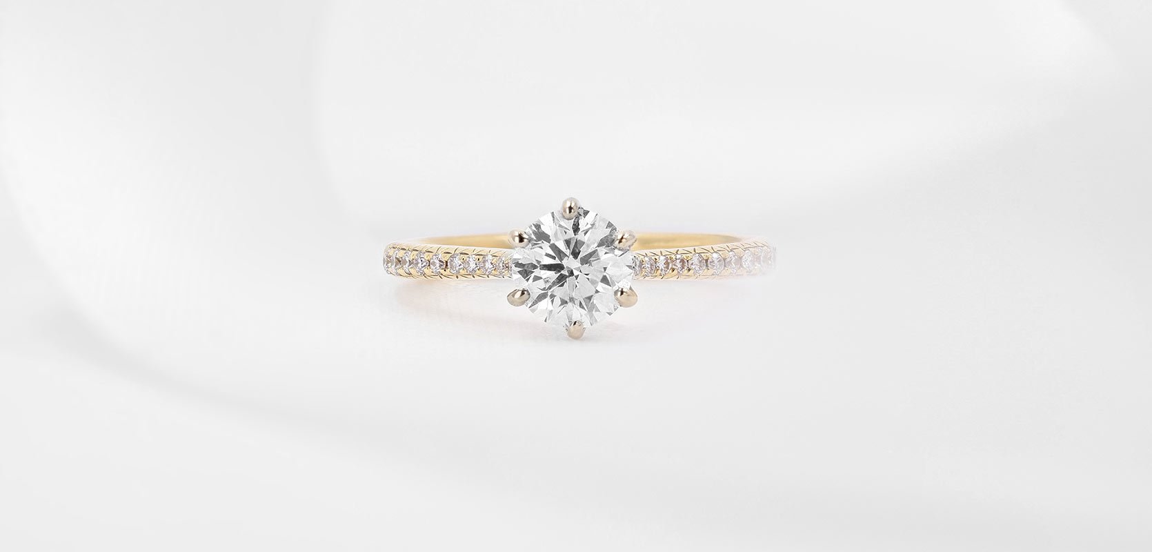 A round brilliant cut diamond engagement ring in 18ct yellow gold with diamond-set shoulders.