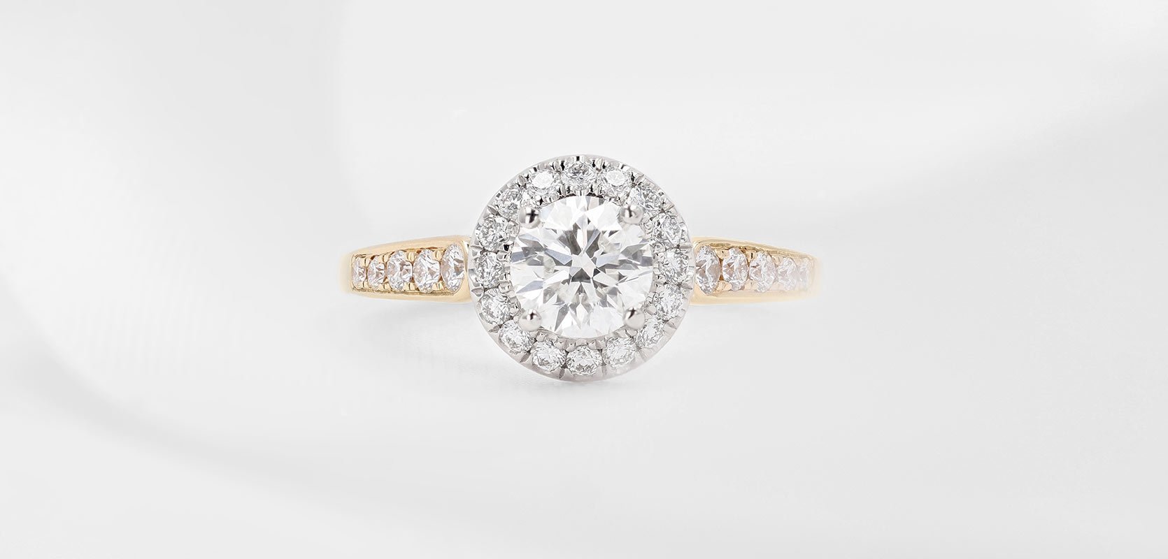 A round brilliant cut diamond engagement ring in 18ct yellow gold with diamond-set shoulders.