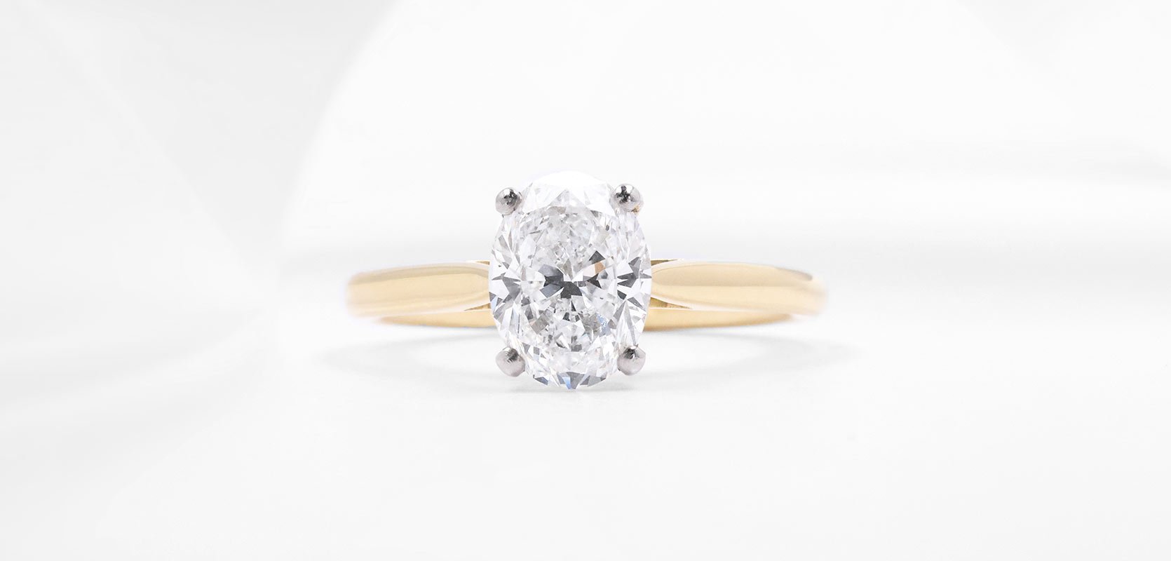 A diamond solitaire engagement ring with an oval cut diamond, set into platinum claws and mounted on an 18ct yellow gold band.