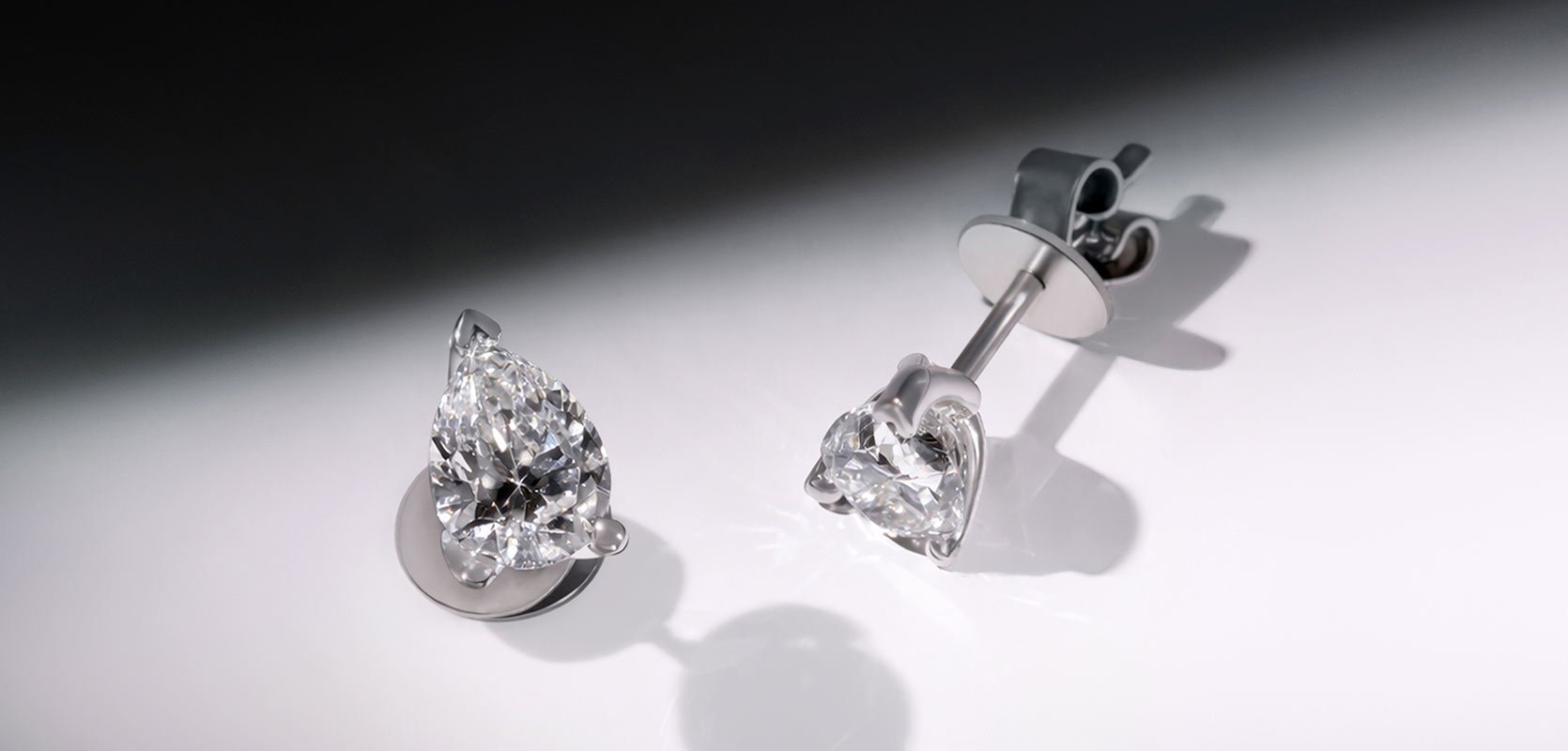 A pair of laboratory grown diamond stud earrings, with two pear cut diamonds held in a platinum claw setting.