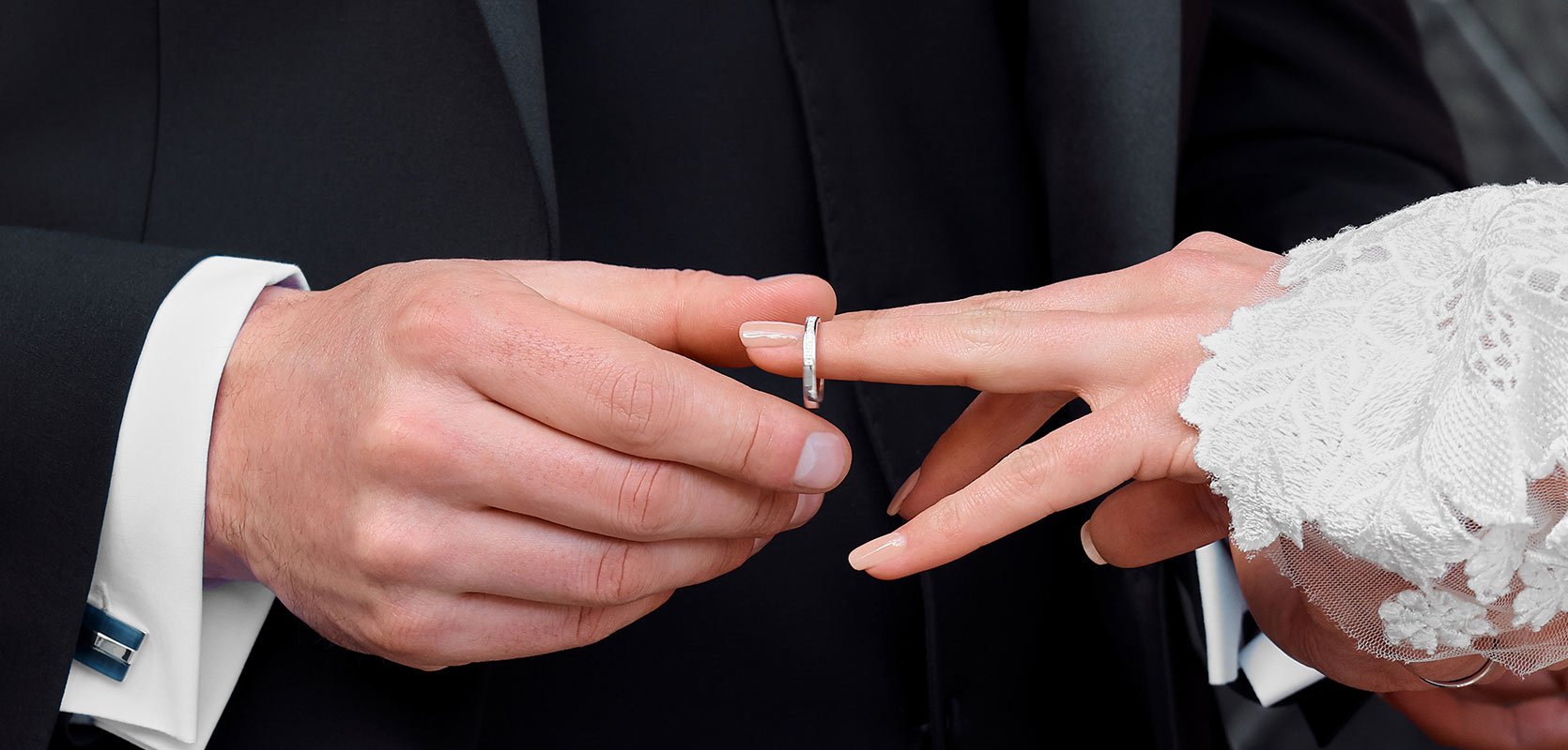 A groom places an 18ct rose gold diamond-set wedding band onto the brides ring finger.