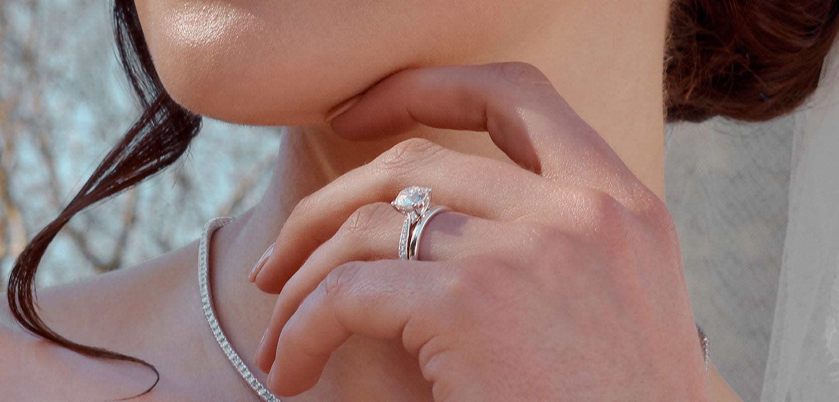 A bride with her solitaire engagement ring that's set with diamond shoulders, and a plain platinum wedding band.