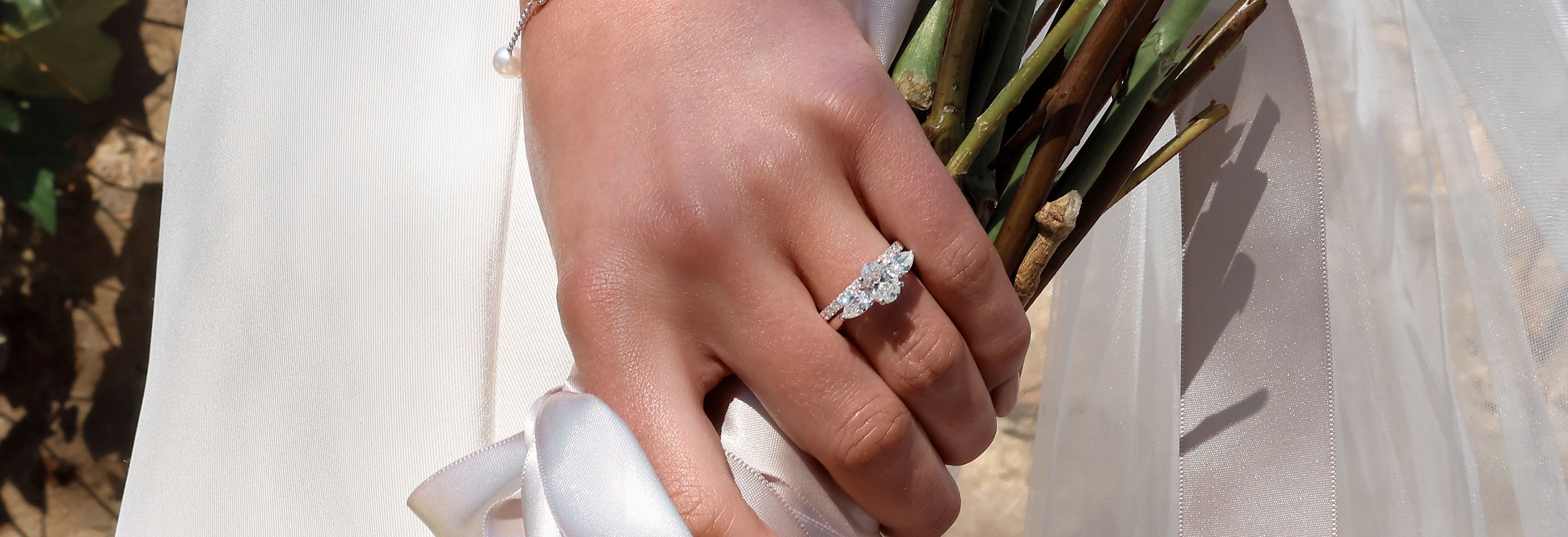A newlywed bride displays her three stone diamond engagement ring, with a diamond set band sitting below, both in platinum.
