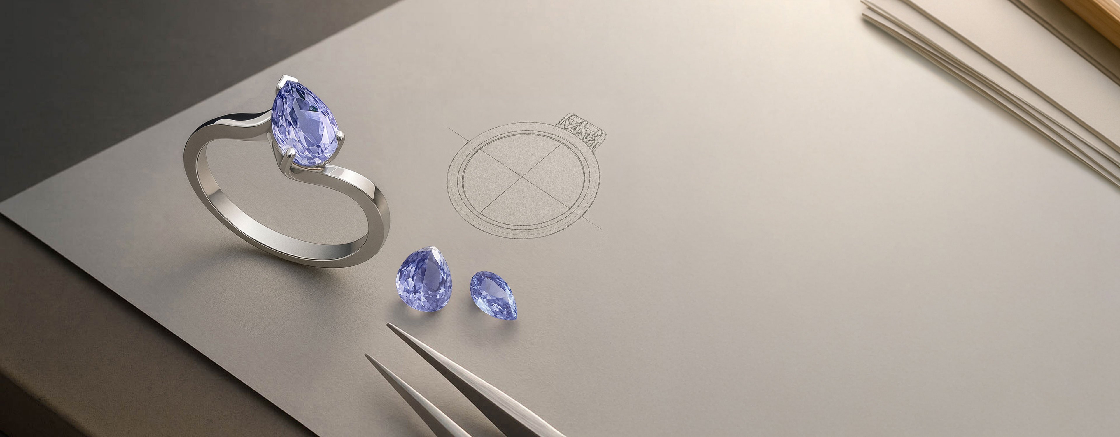 A platinum pear cut gemstone ring sitting beside a few loose gemstones of the same colouring, atop a drawing of the ring itself.