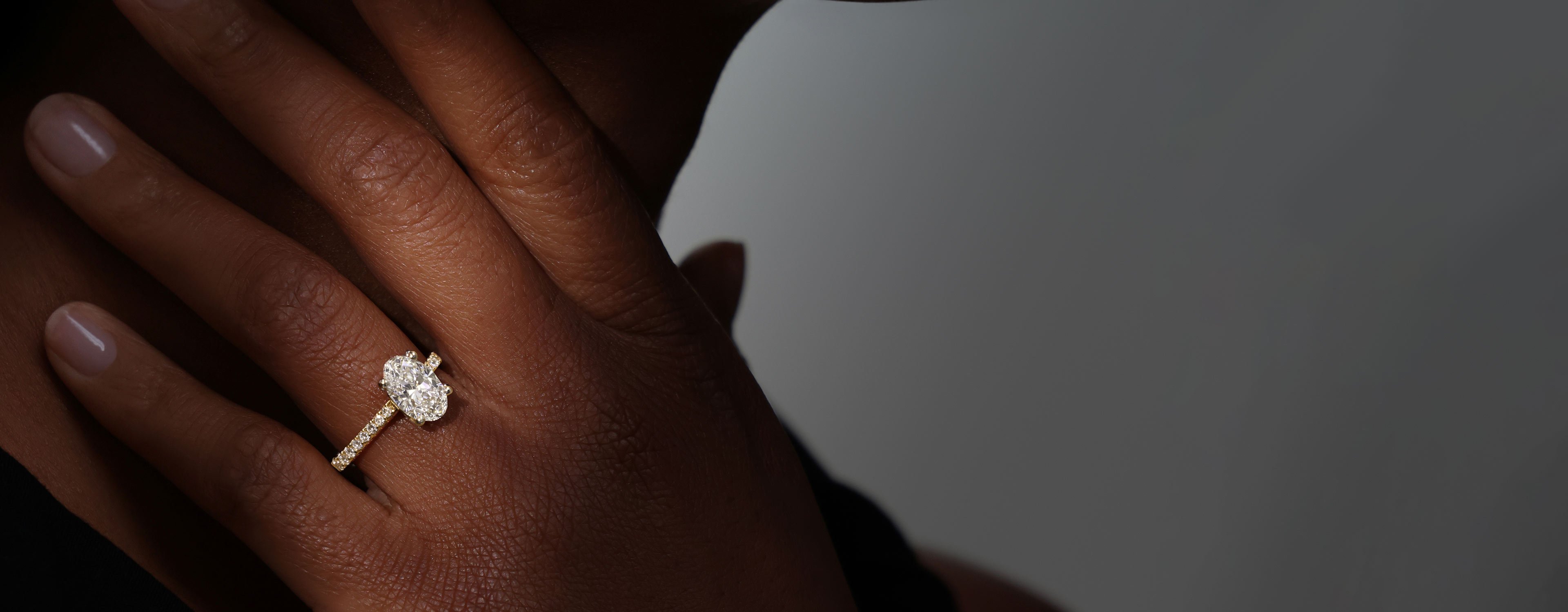 A model wearing an 18ct yellow gold diamond engagement ring, with an oval cut laboratory grown diamond at the centre.