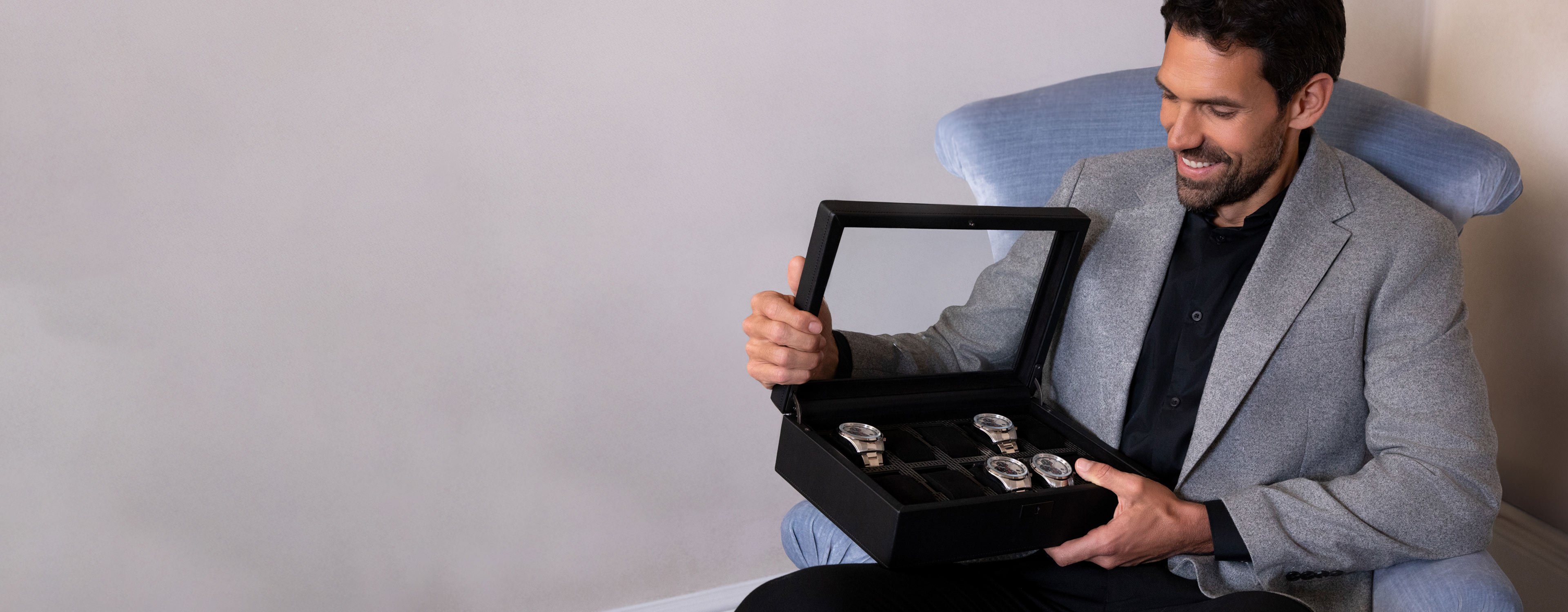 A man sits admiring a WOLF watch box, with four watches within the box.