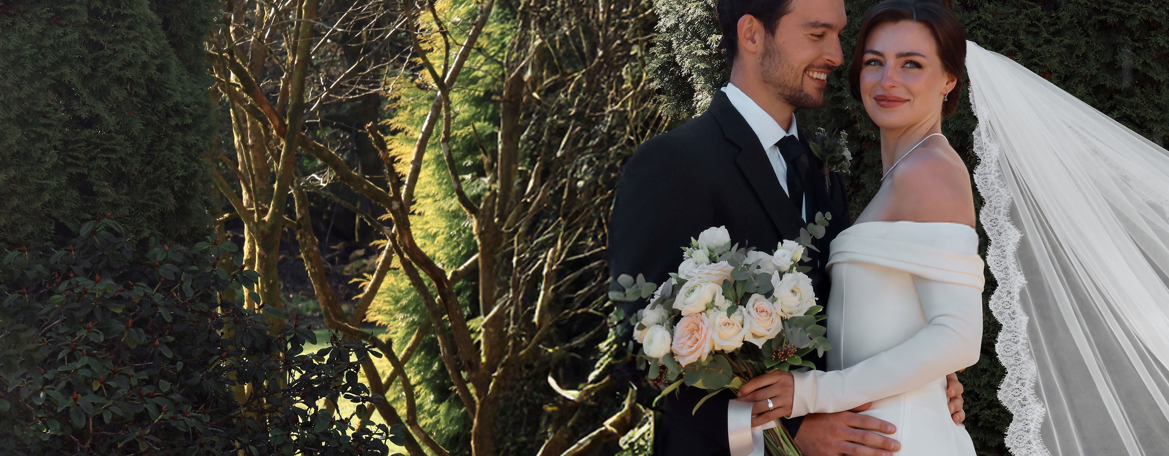 A newlywed bride and groom pose for photographs in the garden. The bride is wearing a diamond engagement ring, platinum wedding band and diamond necklace.