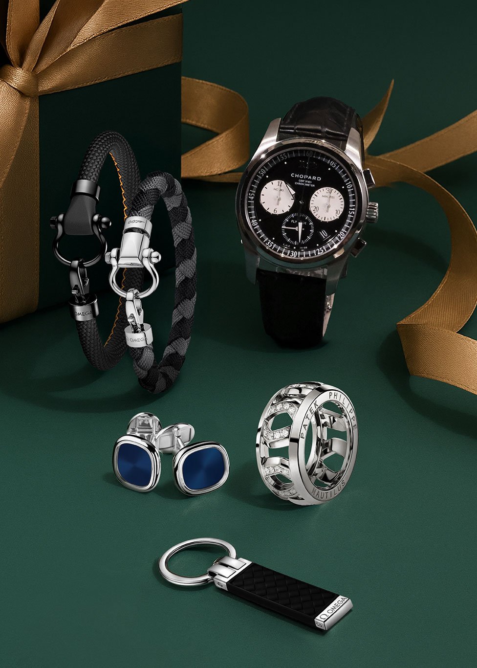 A layout with a green background featuring a mens watch, OMEGA sailing bracelet, OMEGA keyring, cufflinks and men's eternity rings.