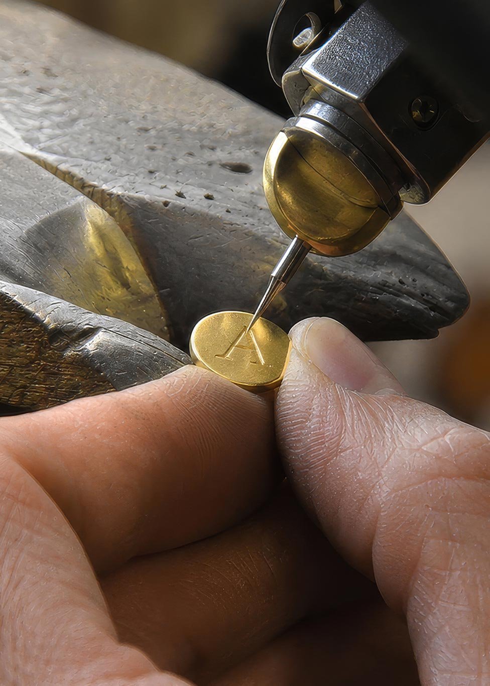 Craftsperson engraving the letter A into a pieces of yellow gold jewellery