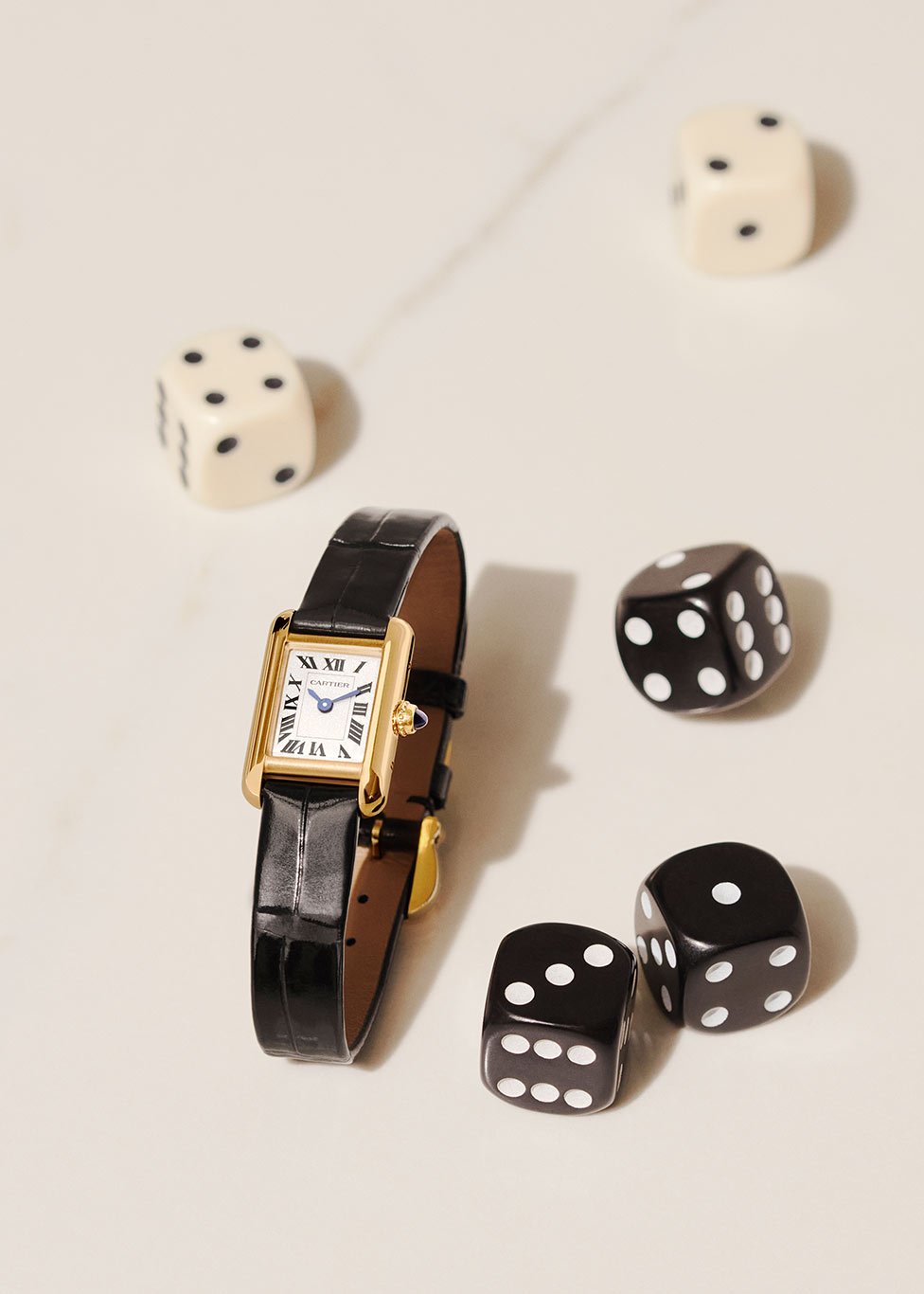 A Cartier tank watch in 18ct yellow gold and alligator leather, with a few dice sitting beside in both cream and black.