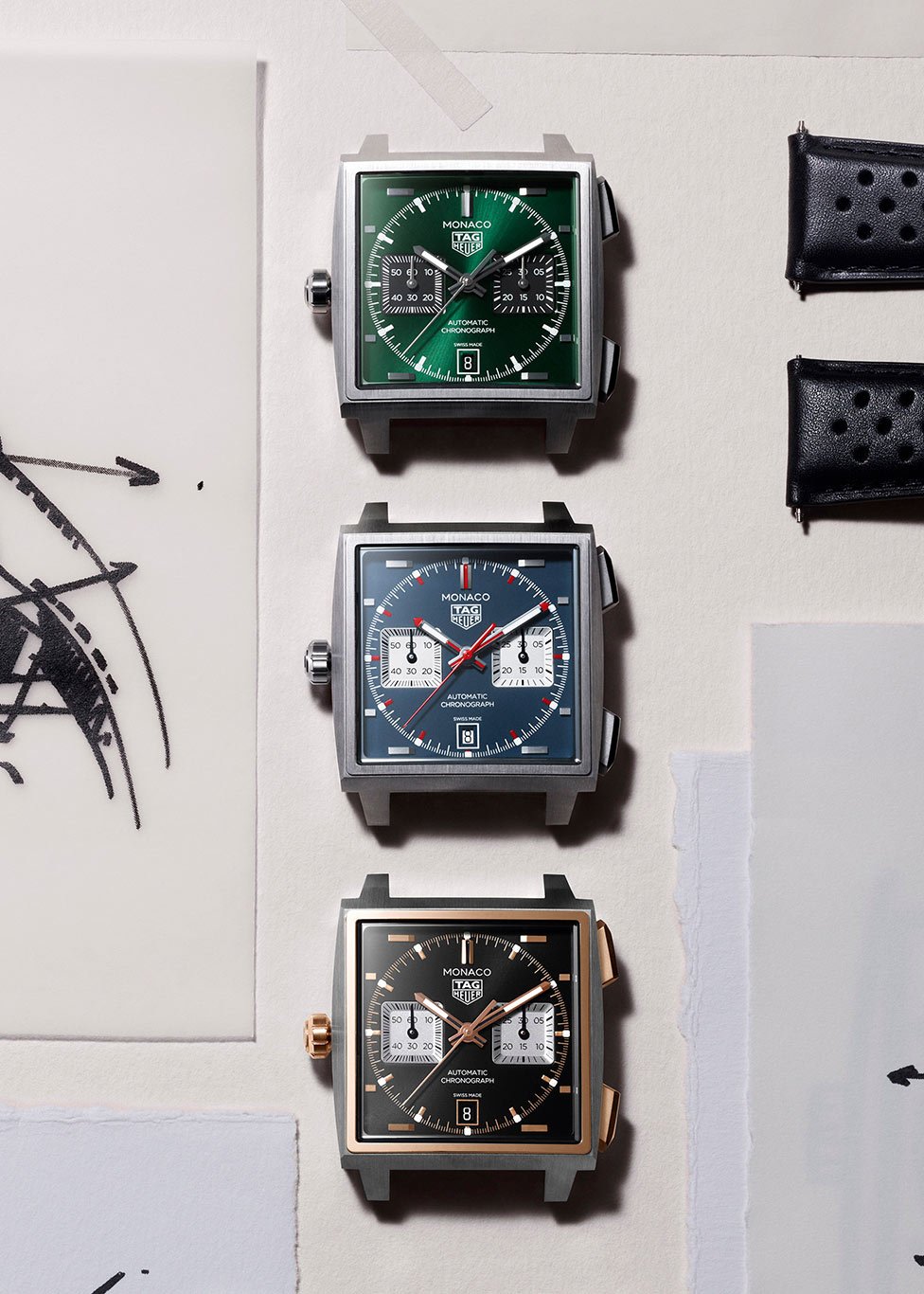 Three TAG Heuer Monaco dials, one green, one blue and one black sitting vertically atop drawings.