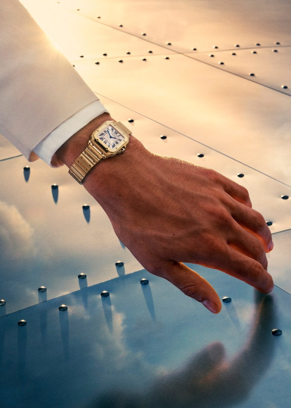 Close-up of a hand wearing a gold wristwatch with a rectangular white dial featuring Roman numeral markers and a linked bracelet.