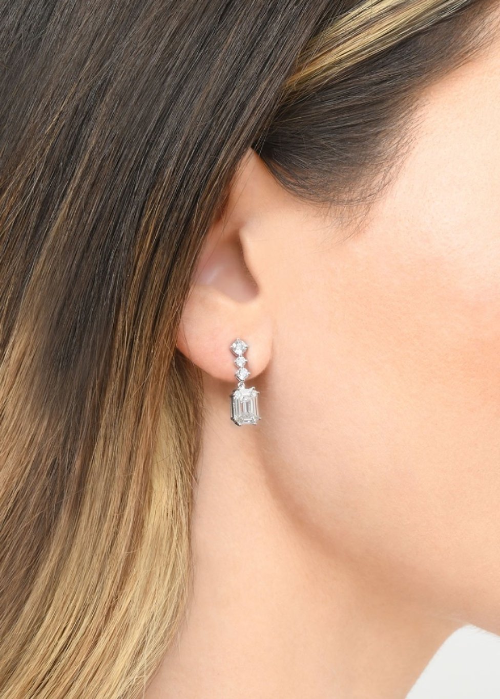 A lady wearing a pair of 18ct white gold diamond drop earrings, with princess cuts cascading down to an emerald cut drop.